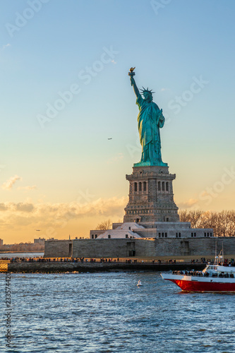 Statue of liberty vertical with red boat during sunset in New York City, NY, USA