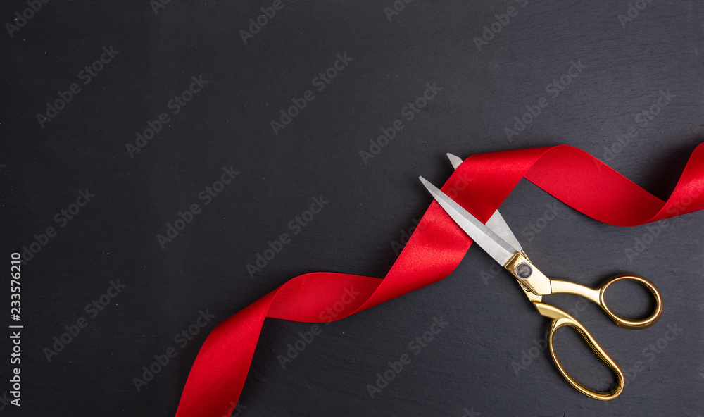 Scissors cutting red silk ribbon against black background - obrazy, fototapety, plakaty 