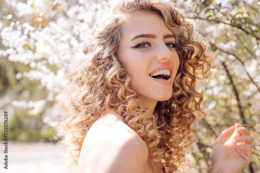 Smiling spring curly girl. Sensual blonde in Blooming flowers in orchard. Spring day concept. Good day. Smiling spring curly girl. Sensual blonde in Blooming flowers in orchard. Spring day concept. Good day.