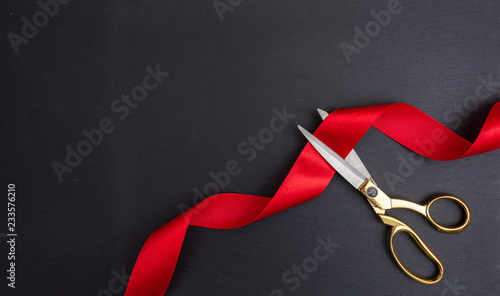 Scissors cutting red silk ribbon against black background