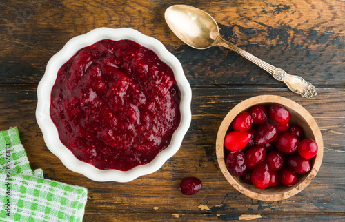 Traditional cranberry sauce in white bowl and fresh berries, top view