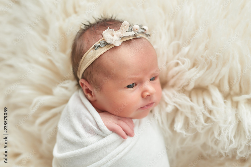 Cute newborn baby girl lies swaddled in a white blanket. Baby goods packaging template. Closeup portrait of newborn baby with smile on face. Healthy and medical concept. Cute newborn baby girl lies swaddled in a white blanket. Baby goods packaging template. Closeup portrait of newborn baby with smile on face. Healthy and medical concept.