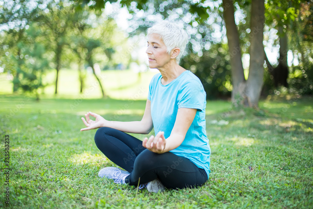 Obraz premium Senior woman in a lotus position on a grass