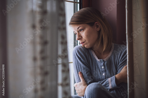 Sad woman sitting by the window looking outside