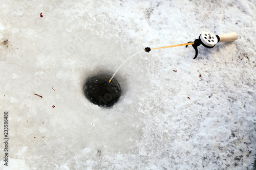 Hole in the ice for winter fishing and a fishing rod with a reel and fishing line and bait. Concept male hobby or sport, tourism and leisure