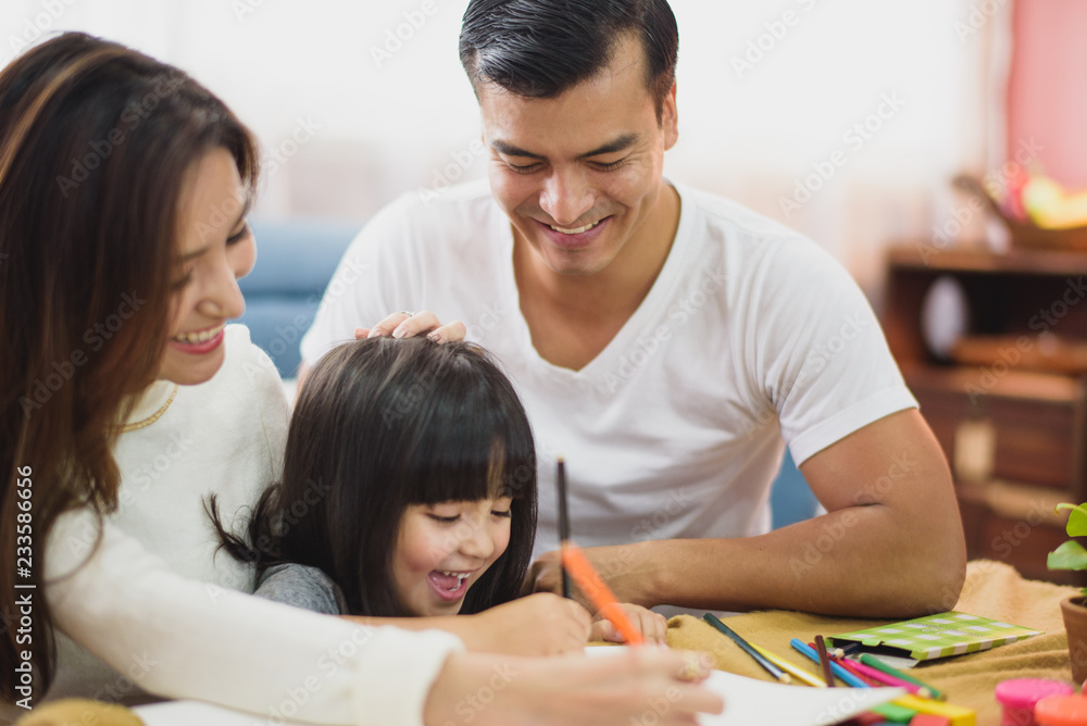 Family time Daughter laughing enjoying writing painting with her father and mother on the table in front of sofa at home. Family time Daughter laughing enjoying writing painting with her father and mother on the table in front of sofa at home.