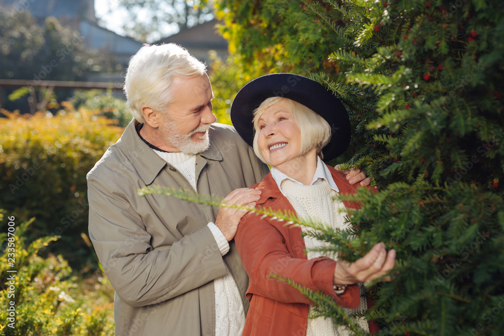 Delighted bearded man putting hands on his wifes shoulders