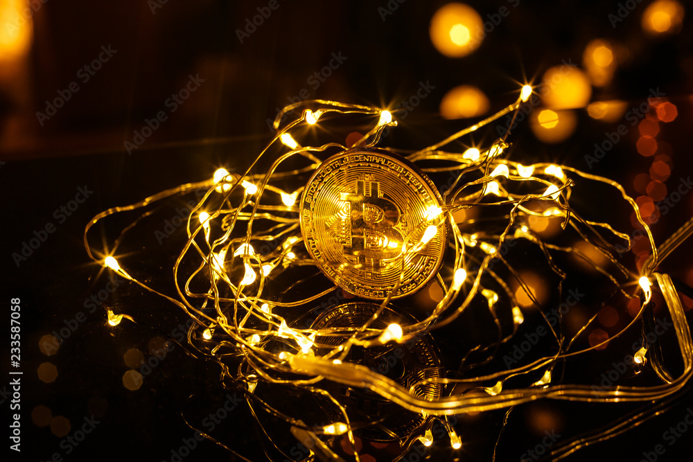 Golden Bitcoin currency. Festive atmosphere. Colorful Christmas tree lights in the background. BTC is a cryptocurrency and is the first decentralized peer-to-peer payment network. Golden Bitcoin currency. Festive atmosphere. Colorful Christmas tree lights in the background. BTC is a cryptocurrency and is the first decentralized peer-to-peer payment network.
