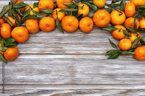 Tangerines (oranges, clementines) with green leaves over wooden background with copy space