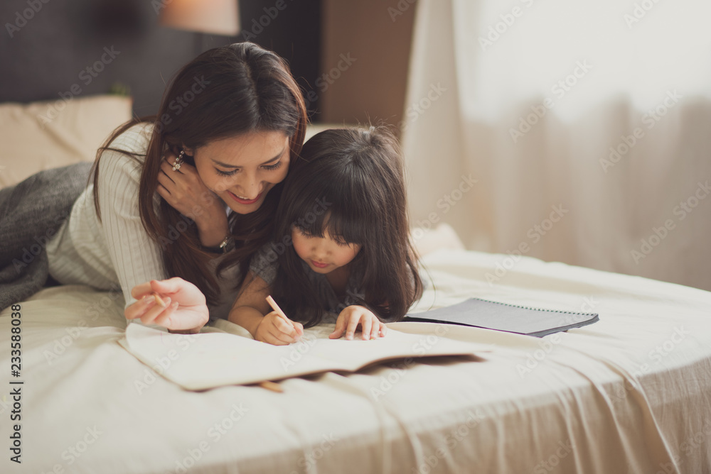 Love of young mother and daughter. Teaching reading a homework or book on the bed at home. mother and daughter look at the book feel good Love of young mother and daughter. Teaching reading a homework or book on the bed at home. mother and daughter look at the book feel good