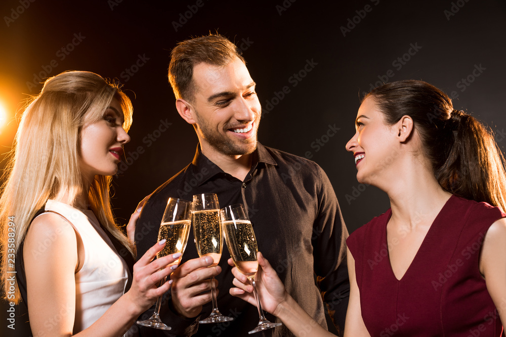 group of happy friends clinking champagne glasses under golden light on black