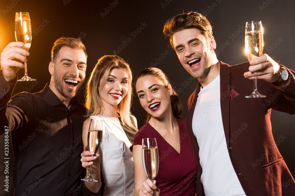 group of friends holding glasses of champagne and looking at camera during party on black