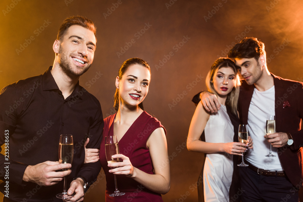 happy young couples with champagne glasses standing under golden light during party