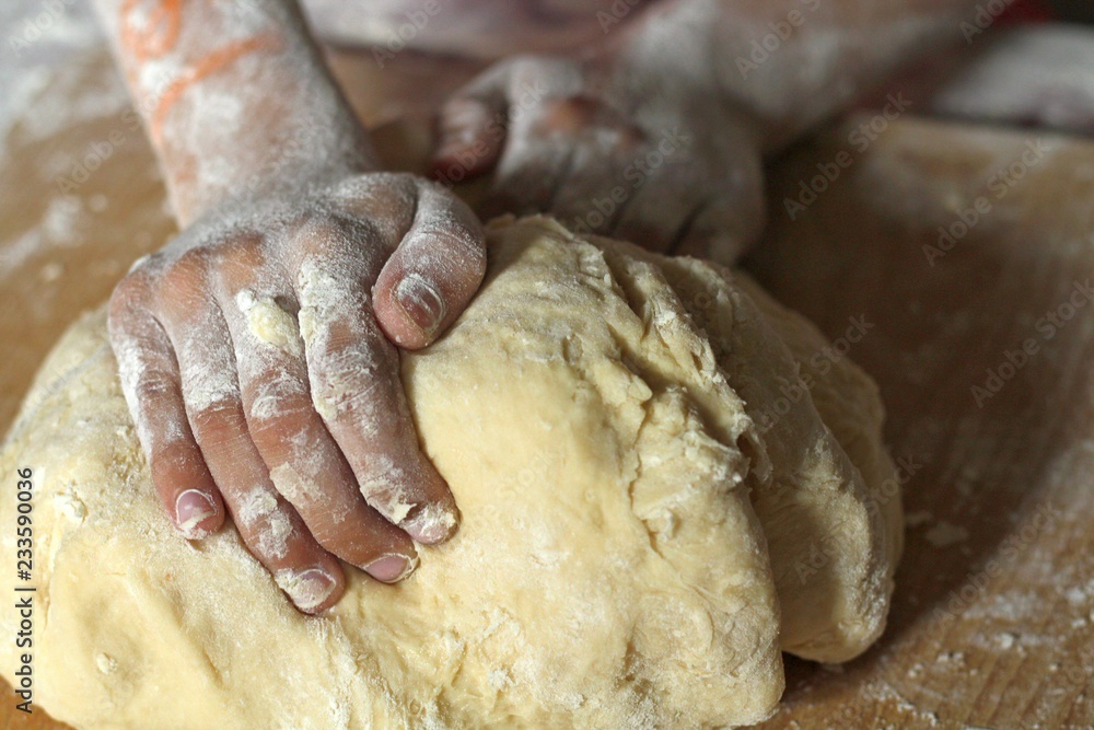 Fototapeta premium The hands of a girl or daughter knead the dough in the kitchen on a wooden board