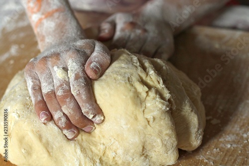 The hands of a girl or daughter knead the dough in the kitchen on a wooden board