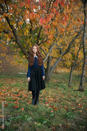 Red-hair girl dancing and playing in the autumn garden full of colorful leaves.