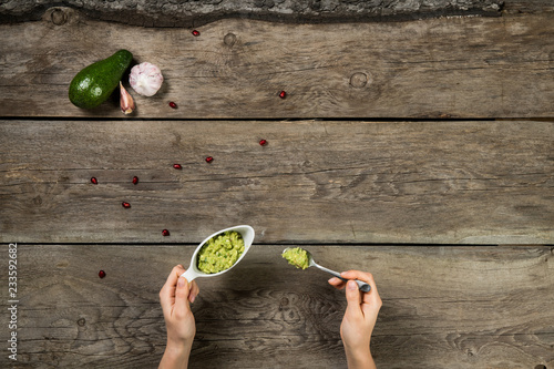 Woman hands holding gravy boat and small spoon with gucamole sauce on wooden background photo