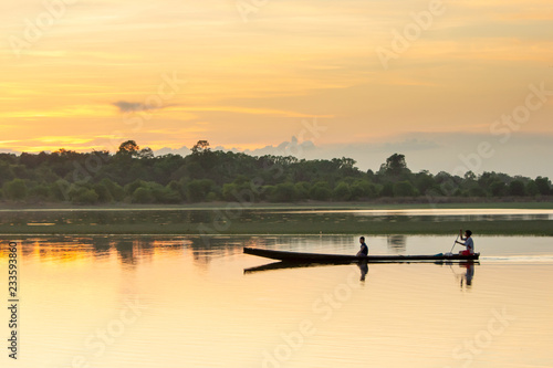 NAKHON PHANOM, THAILAND - OCT 23, 2018 : Father and son paddle wooden boat in the lake for fishing wih sunset background