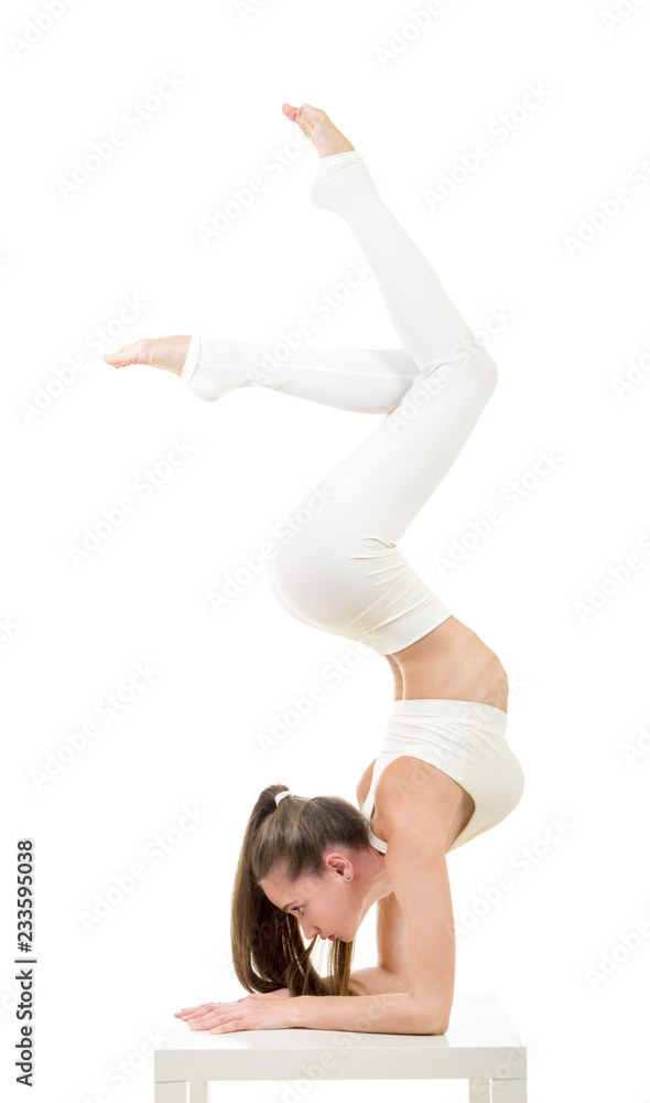 A young woman in a white suit performs acrobatic elements and yoga.