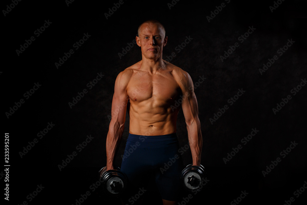 Handsome muscular man working out with dumbbells over black background. Handsome muscular man working out with dumbbells over black background.