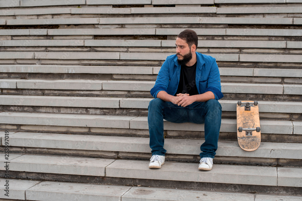 Young skater with beard chilling on the concrete steps Young skater with beard chilling on the concrete steps