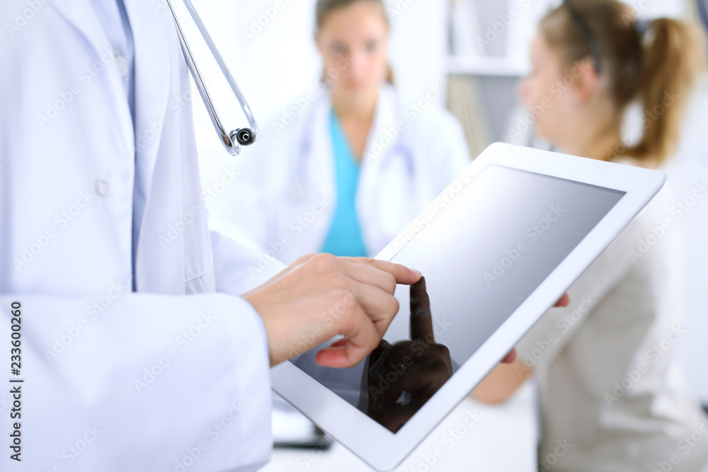 Doctor using tablet computer, close-up of hands at touch pad screen. Patient is at the background Doctor using tablet computer, close-up of hands at touch pad screen. Patient is at the background