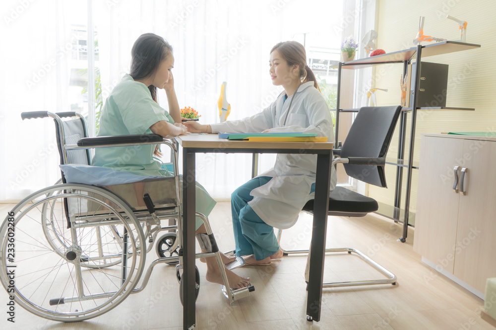 Doctor talking or discussing something while is examining disabled a Asian woman patient sitting on wheelchair for regular check.  Professionalism,Medicine and health care concept. Doctor and patient