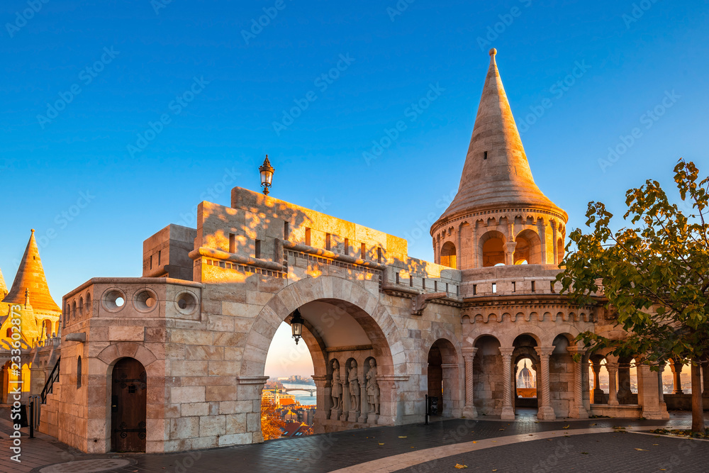 Budapest, Hungary - Entrance and tower of the famous Fisherman's Bastion on a golden autumn sunrise with Parliament of Hungary at the background and clear blue sky