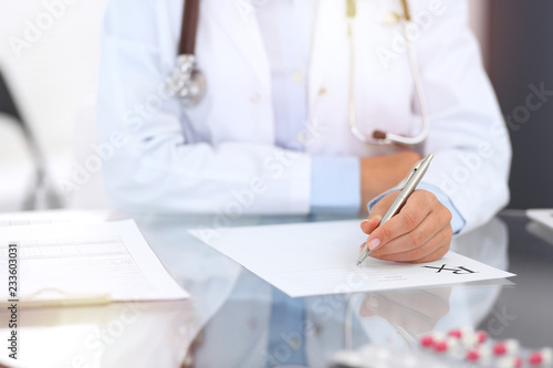 Doctor woman filling up prescription form while sitting at the desk in hospital close-up. Physician at work and ready to give an advice to help patient. Healthcare, insurance and excellent service i