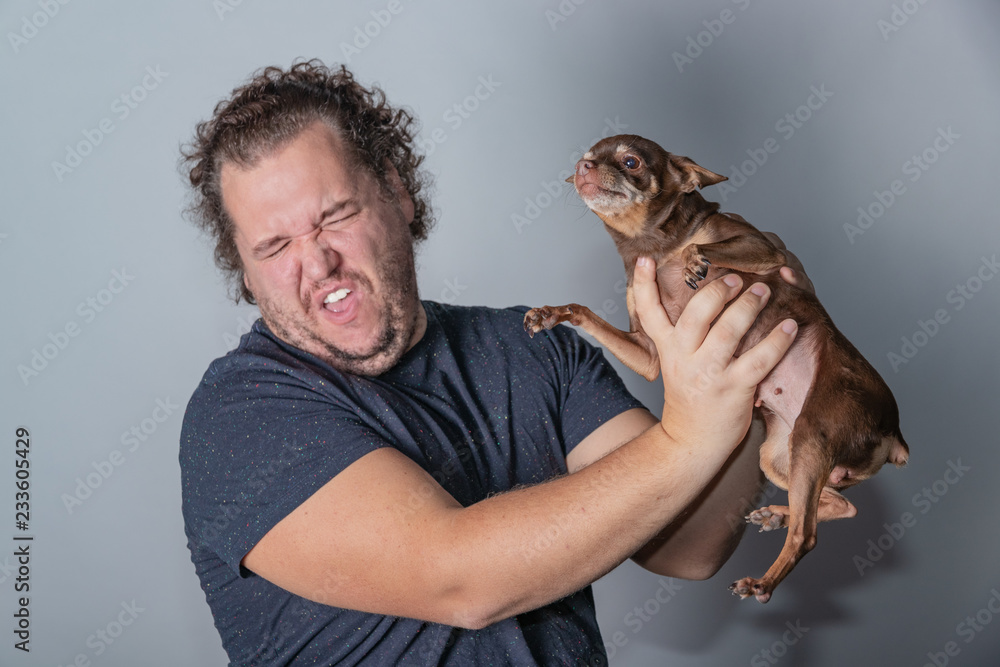 Obraz premium Funny fat man poses with little dog on gray background