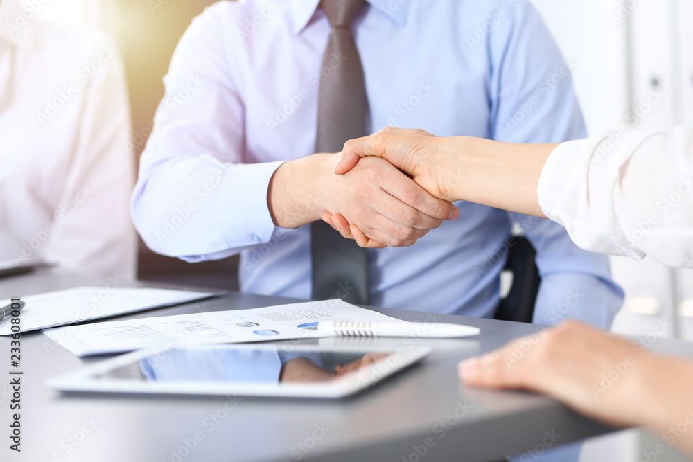 Close-up of business handshake at meeting or negotiation above the desk in office. Partners shaking hands while satisfied because signing contract or financial papers. Success concept Close-up of business handshake at meeting or negotiation above the desk in office. Partners shaking hands while satisfied because signing contract or financial papers. Success concept