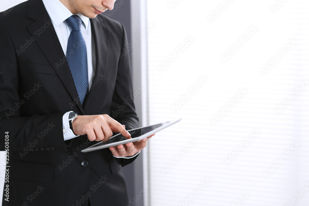 Businessman using digital tablet while standing near window in office, close-up. Copy space area Businessman using digital tablet while standing near window in office, close-up. Copy space area