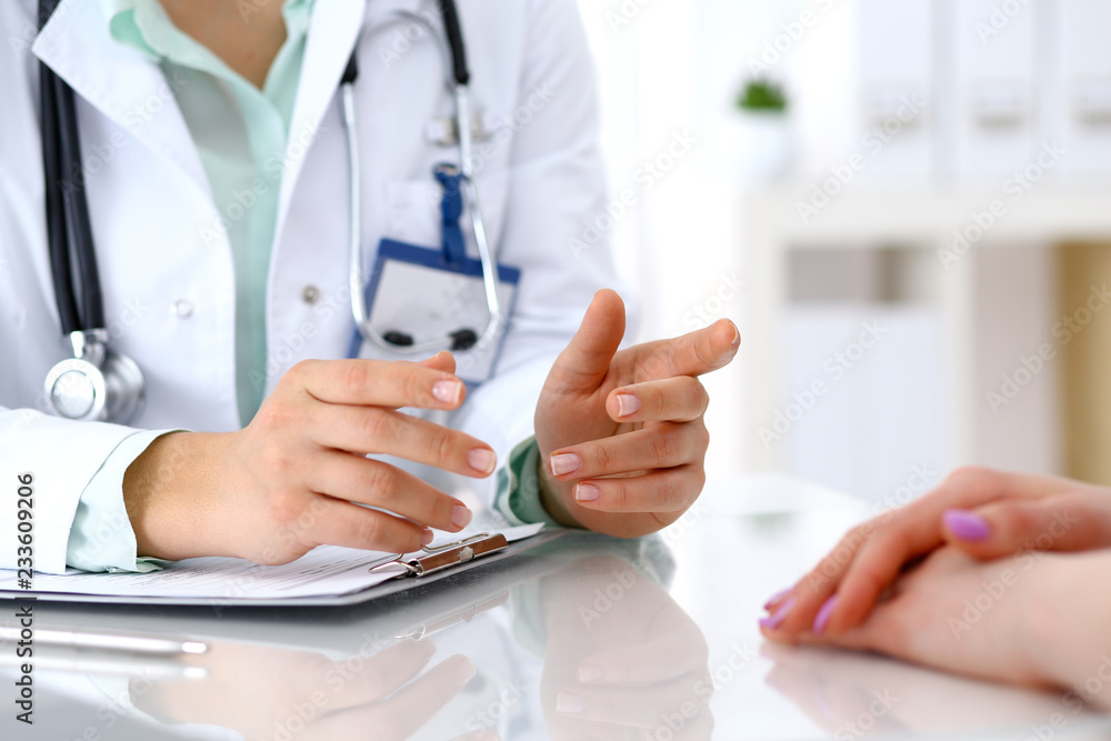 Doctor and patient talking while sitting at the desk in hospital office, close-up of human hands. Medicine and health care concept Doctor and patient talking while sitting at the desk in hospital office, close-up of human hands. Medicine and health care concept