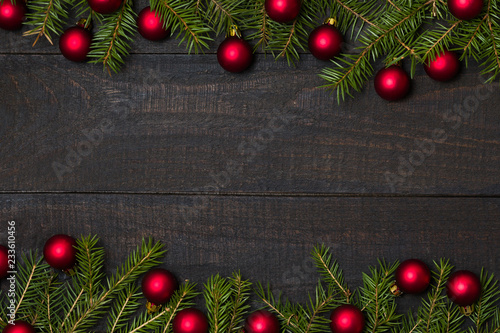 Dark rustic wooden table background with Christmas decoration -  fir and red ornament frame. Top view with free space for copy text
