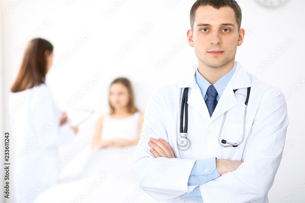 Medicine doctor standing and smiling on the background with patient in the bed Medicine doctor standing and smiling on the background with patient in the bed