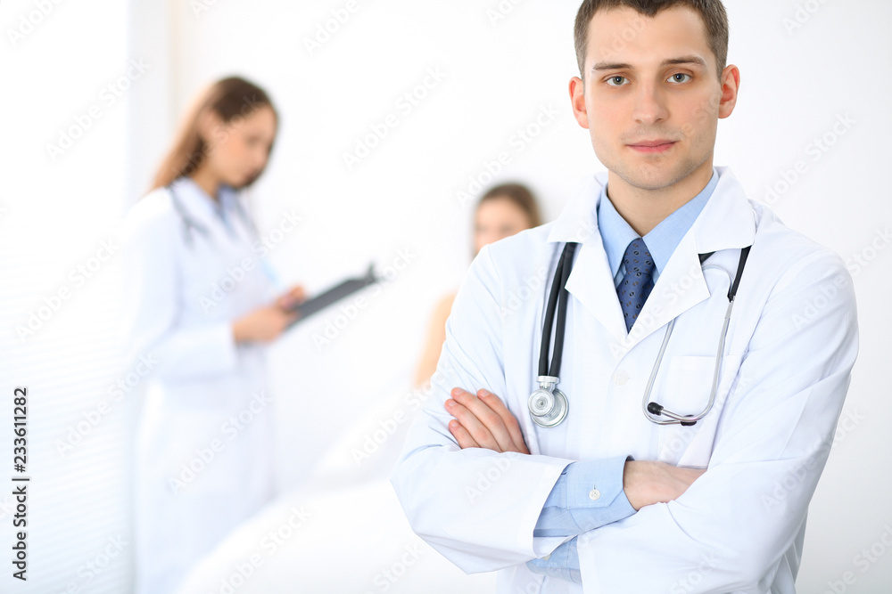Medicine doctor standing and smiling on the background with patient in the bed Medicine doctor standing and smiling on the background with patient in the bed