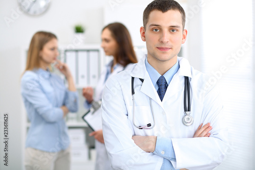 Friendly male doctor on the background with patient and physician