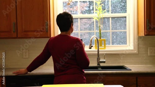  A woman holds a cup of coffee while looking outside at the falling snow from inside her warm home