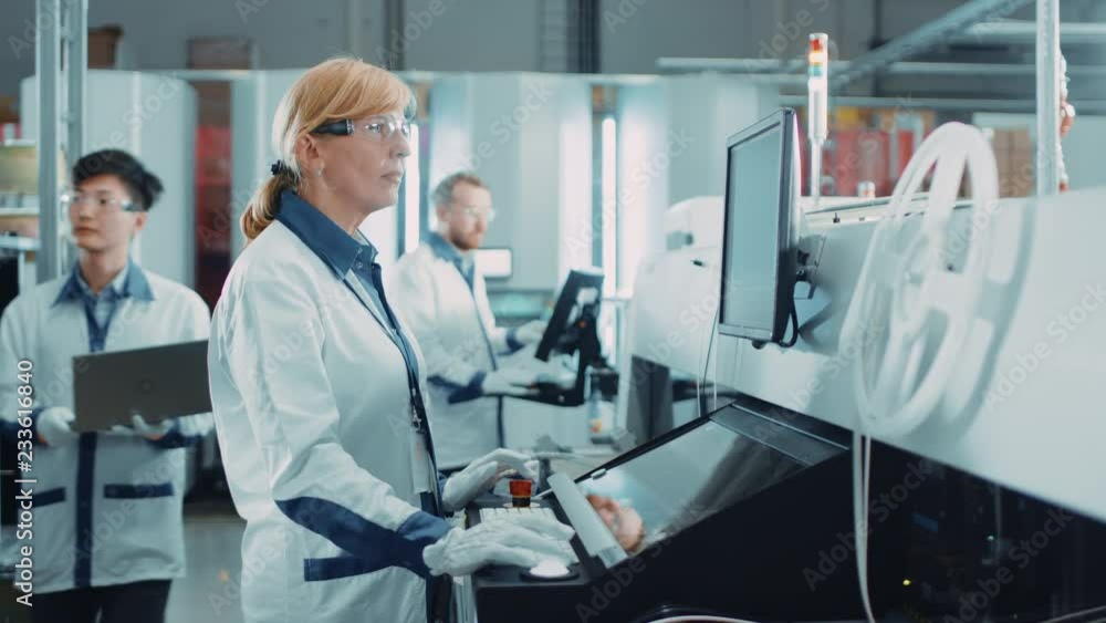 On High Tech Factory Female Engineer Uses Computer for Programing Pick and Place Electronic Machinery for Printed Circuit Board Surface Mount Assembly Line. Production of PCB with SMT Machinery. On High Tech Factory Female Engineer Uses Computer for Programing Pick and Place Electronic Machinery for Printed Circuit Board Surface Mount Assembly Line. Production of PCB with SMT Machinery.