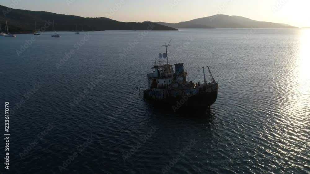 Aerial view. Flying around an old rusty abandoned sunken ship at dawn at low altitude. The skeleton of a merchant ship stranded in the Bay against the mountains. Aerial view. Flying around an old rusty abandoned sunken ship at dawn at low altitude. The skeleton of a merchant ship stranded in the Bay against the mountains.