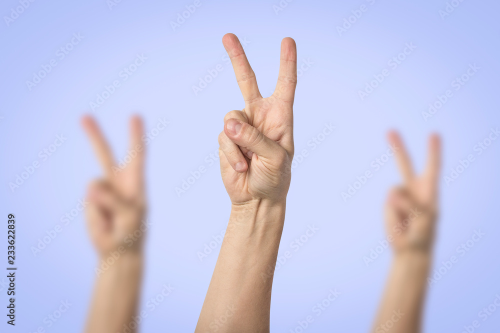 Male hands raised up and showing a gesture of peace with two lifted fingers on a blue background. Gesture Yo. Concept of power, unity, rap respect Male hands raised up and showing a gesture of peace with two lifted fingers on a blue background. Gesture Yo. Concept of power, unity, rap respect