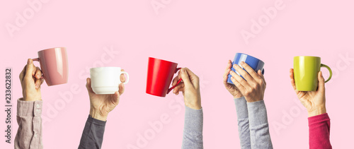 Many different hands holding multi colored cups of coffee on a pink background. Female and male hands. Concept of a friendly team, a coffee break, meeting friends, morning in the team. Banner