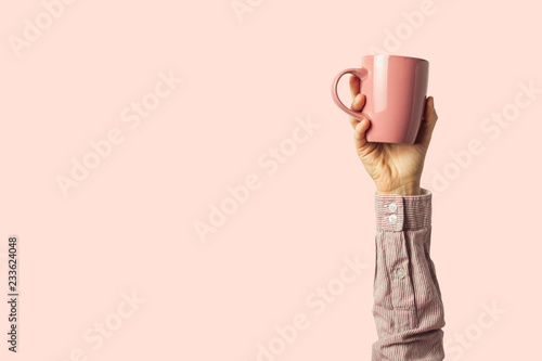 Female hand holding a purple cup with hot coffee or tea on a light pink background. Breakfast concept with hot coffee or tea