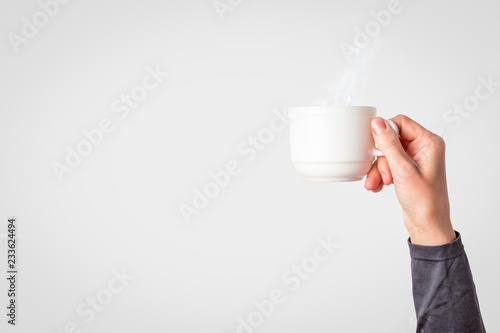 Female hand holding a white cup with hot coffee or tea on a light blue background. Breakfast concept with hot coffee or tea