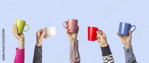 Many different hands holding multi colored cups of coffee on a blue background. Female and male hands. Concept of a friendly team, a coffee break, meeting friends, morning in the team. Banner