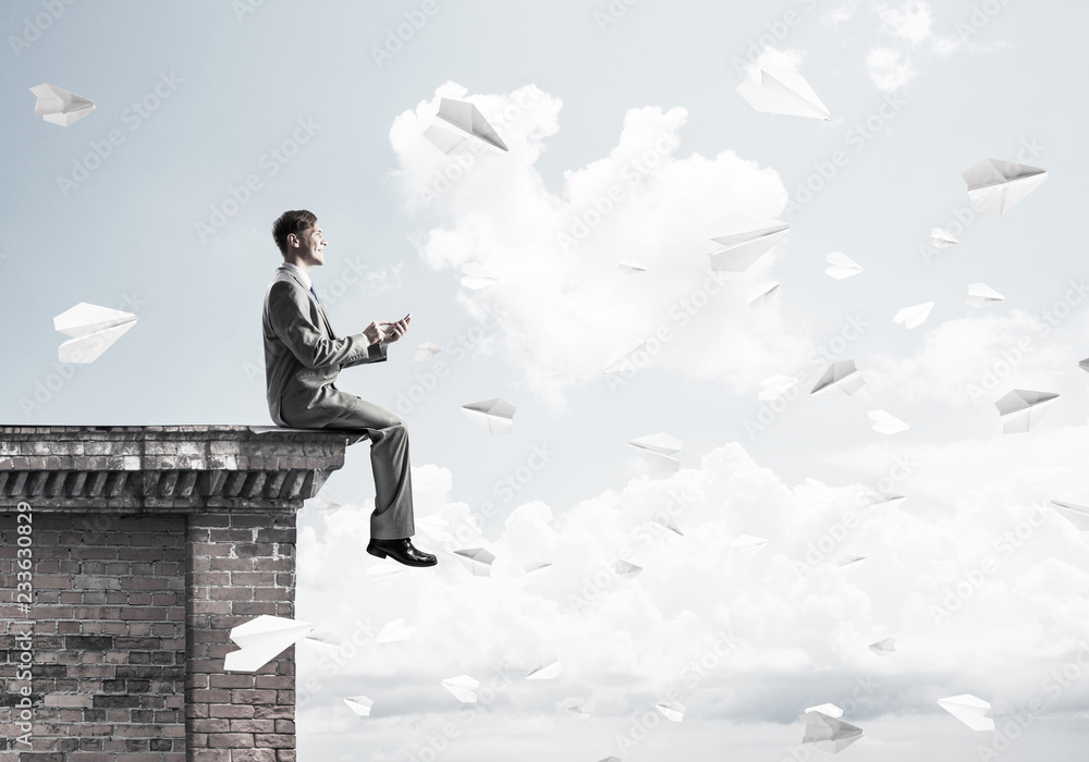 Man on roof edge send message with smartphone and cityscape at b Man on roof edge send message with smartphone and cityscape at b