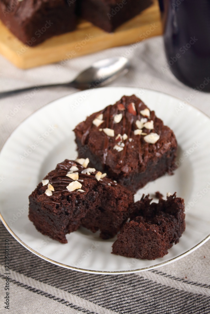 Chocolate fudgy brownie with nuts on white plate with spoon