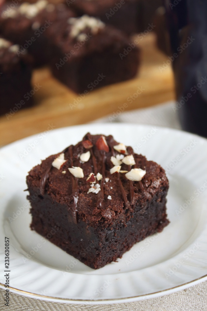 Chocolate fudgy brownie with nuts on white plate with spoon Chocolate fudgy brownie with nuts on white plate with spoon