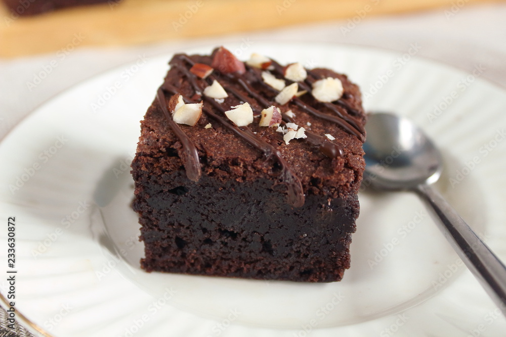 Chocolate fudgy brownie with nuts on white plate with spoon