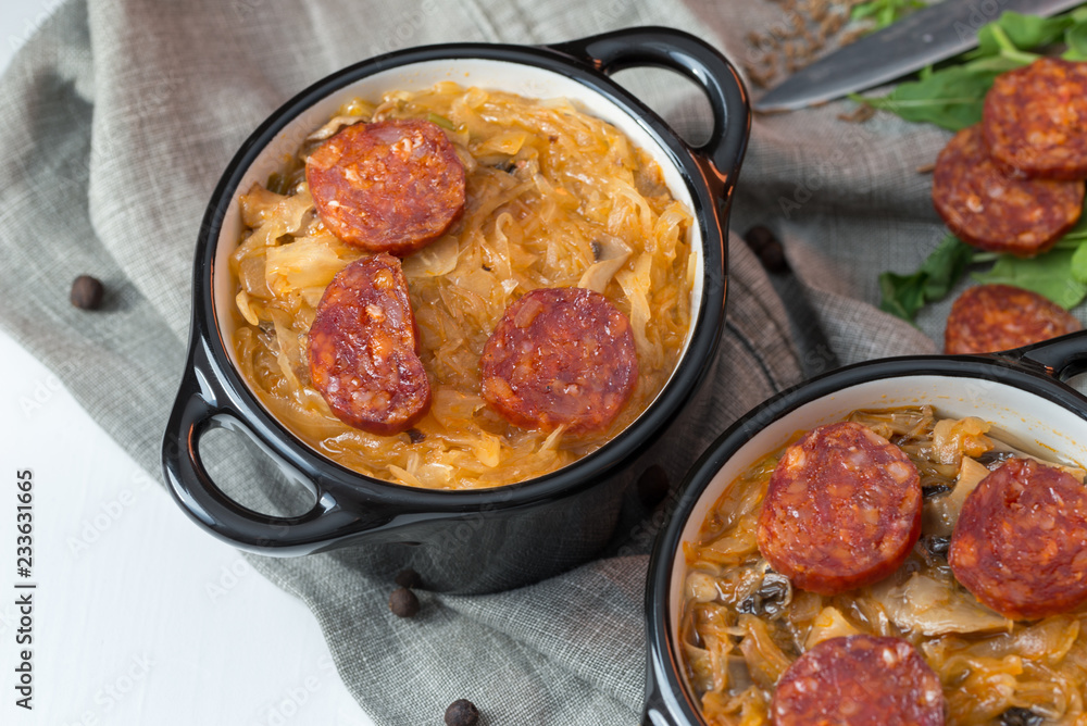 Slovak Christmas national cabbage soup in two small black pots with sausage on the tablecloth background. Slovak Christmas national cabbage soup in two small black pots with sausage on the tablecloth background.